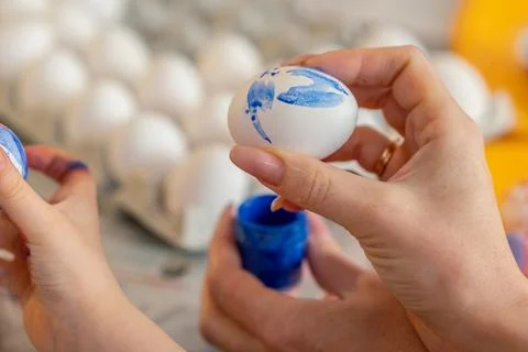 Happy Easter. Mom holds Easter egg painted by her daughter. Kid draws blue and Stock Photos