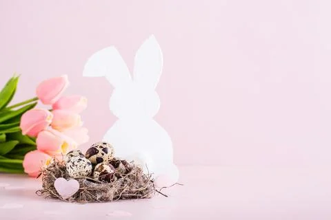 Happy easter quail eggs in a nest, white rabbit and tulips on a pink backgr.. Stock Photos