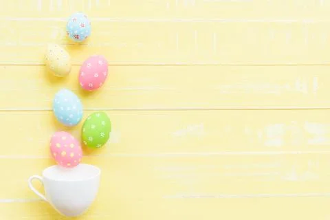 Happy easter! Row colorful Easter eggs spread out from white cup on bright ye Stock Photos