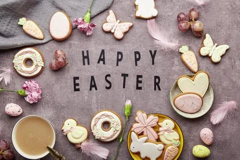 Happy Easter text among decorated Easter cookies, pink flowers, coffee cup and Stock Photos