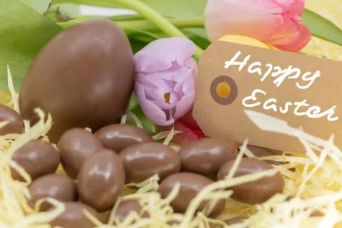 Happy Easter text with chocolate eggs for Easter and pastel tulips Stock Photos