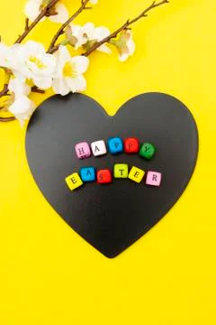 Happy Easter text on heart shaped blackboard, yellow spring background with f Stock Photos
