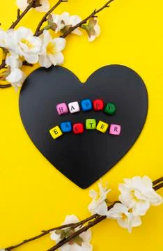 Happy Easter text on heart shaped blackboard, yellow spring background with f Stock Photos