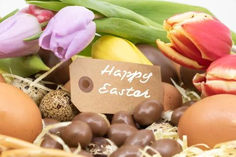 Happy easter text on a label surrounded by different Easter eggs and tulips Stock Photos