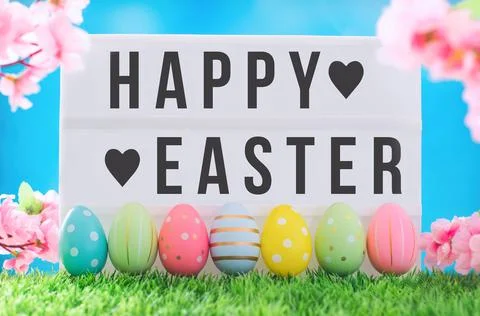Happy Easter text On light box against bright blue sky and flowers. Stock Photos