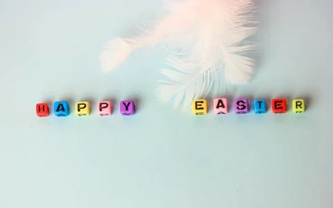 Happy Easter text made of multicolored letters, a feather on a blue backgroun Foto stock