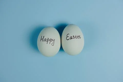Happy Easter text on two white eggs isolaed on blue background. Easter greeting Stock Photos