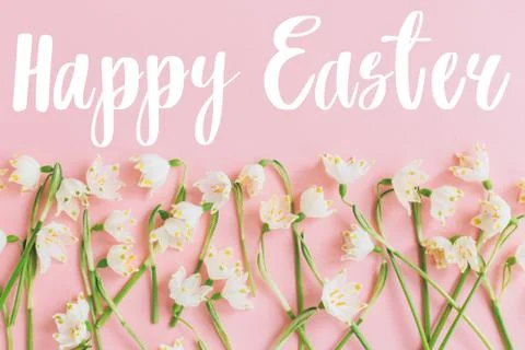 Happy Easter text on white spring flowers on pastel pink flat lay. Stylish ea Stock Photos