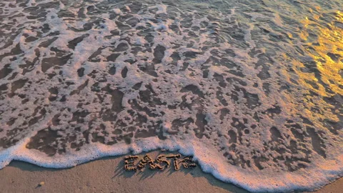 Happy Easter Text Written on Sand Partially Washed Away by a Gentle Wave Slow Mo Stock Footage 331447936
