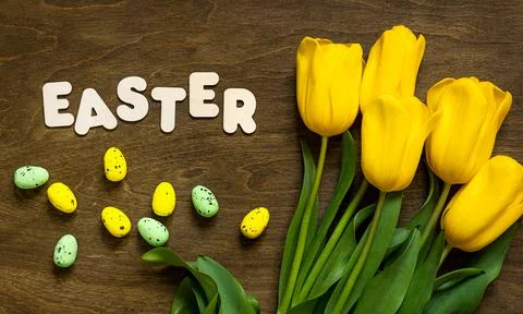 Happy Easter text with yellow tulips and easter eggs on wooden background Stock Photos