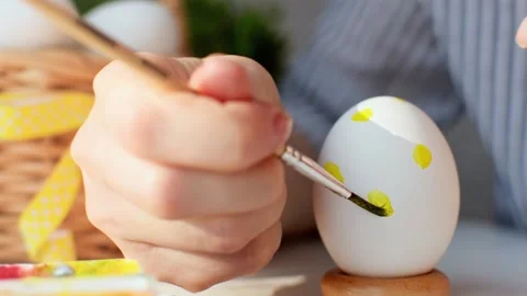 Happy Easter. Young womans hand draws a yellow dots pattern on a chicken egg. 스톡 동영상 236476691