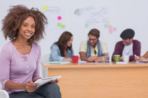 Happy editor using tablet as team works behind her Stock Photos