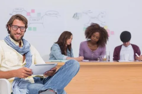 Happy editor using tablet as team works behind him Stock Photos