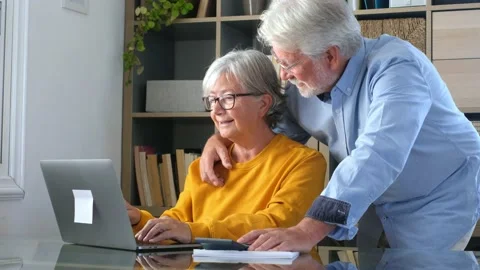 Happy elderly 60s couple sit rest on couch at home pay household expenses online Stock Footage 152111374