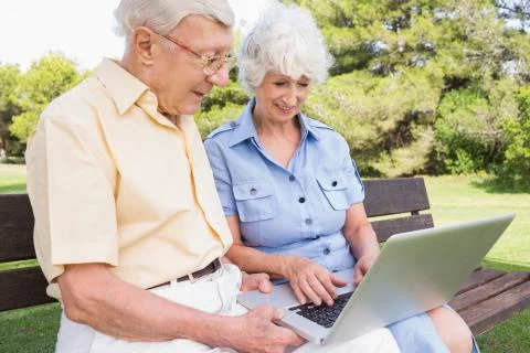 Happy elderly couple in the park using a laptop Photos