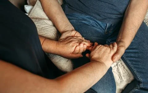 Happy elderly couple sit side by side holding hands. Stock Photos