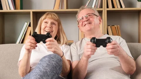 Happy elderly couple sitting on the sofa at home, they are playing games holding Stock-Footage 252685694