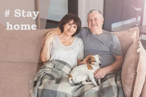 Happy elderly couple sitting on sofa at home during the pandemic coronavirus Stock Photos