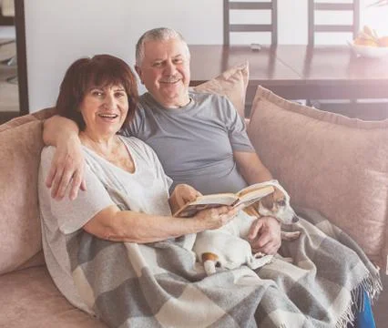 Happy elderly couple sitting on sofa at home Stock Photos