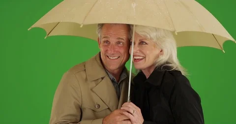 Happy elderly couple standing in the rain with an umbrella on green screen Stock Footage