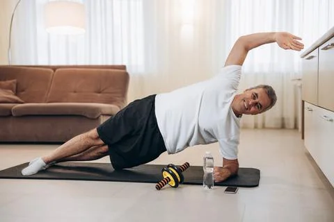 Happy elderly man doing side plank exercise with raised hand, smiling and Foto stock