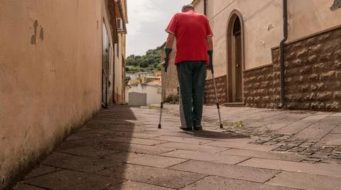 An happy elderly man walking down the street and alleys on crutches, doing Stock Photos