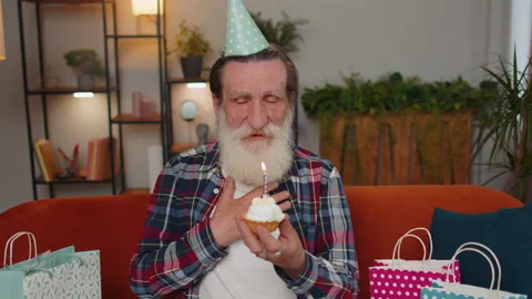 Happy elderly old man celebrating birthday party, makes wish blowing burning Stock Footage