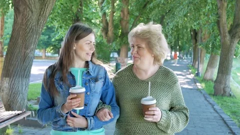 Happy elderly woman adn young woman walking park lane drinking coffee. Stock Footage
