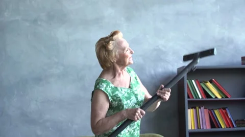 Happy elderly woman dancing with a vacuum cleaner, home fun Stock Footage