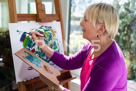 Happy elderly woman painting for fun at home Stock Photos