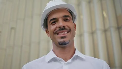 Happy engineer posing modern architecture portrait. Latin man taking off hardhat Stock Photos