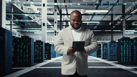 Happy engineer walking in data center refining algorithms on tablet Stock Footage 311963449