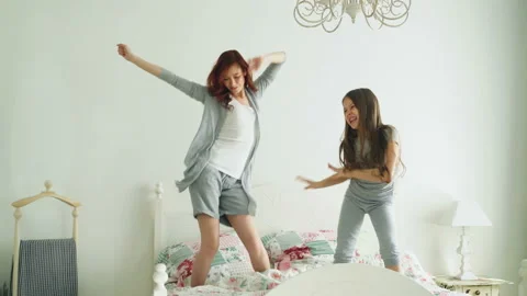 Happy family of cute daughter and young mother jumping and dancing on bed while Stock Footage