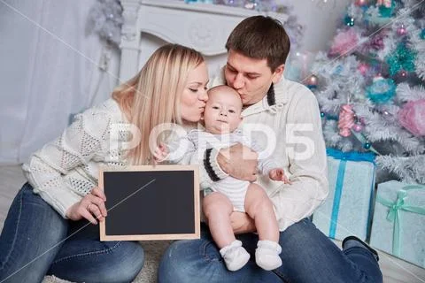 Happy family holding a blank Christmas card, sitting on the carpet in a cozy Stock Photos