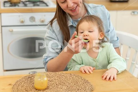 Happy family at home. Mother feeding her baby girl from spoon in