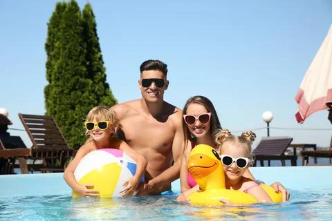 Happy family with inflatable ring and ball in outdoor swimming pool on sunny  Stock Photos