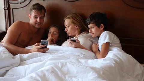 A happy family is looking at something on their smartphone while lying in bed Stock Footage