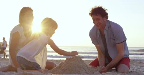 Happy family playing on the beach building sand castle at sunset Stock Footage