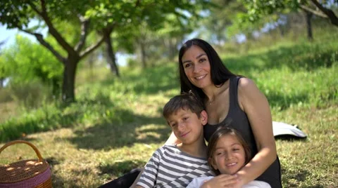 Happy family sitting in a park under trees, looking at camera and smiling. Stock Footage