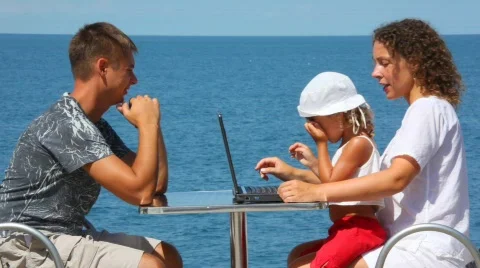 Happy family of three persons with notebook sits at table, sea Stock Footage