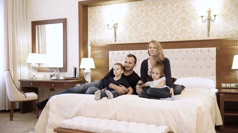 A happy family watching television in hotel room sitting on bed Stock Footage