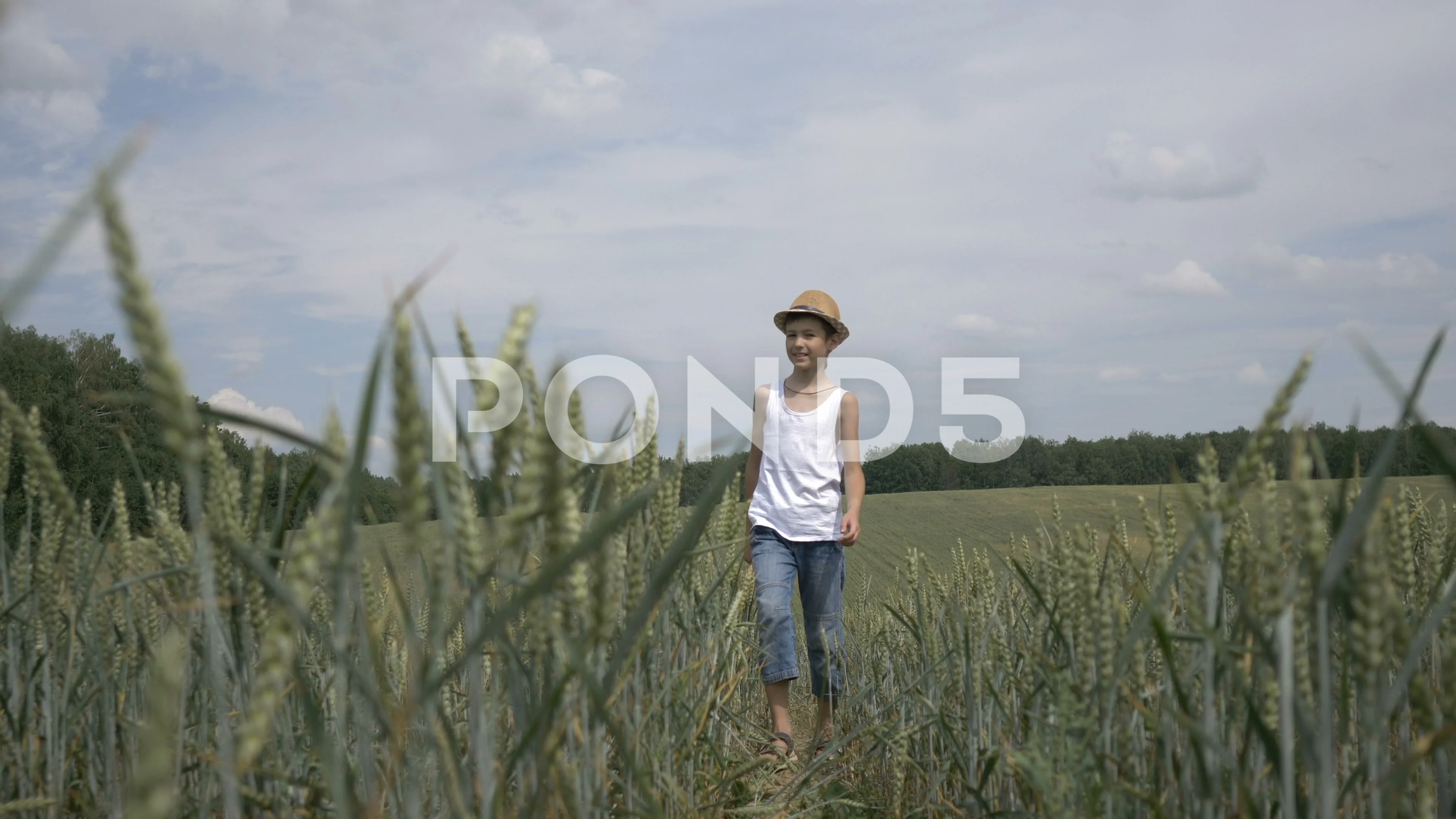 happy farmer boy in a hat is walking across the field, outdoors