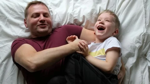 Happy father having fun on a bed with his son child, laughing. View from above Stock Footage 131174100
