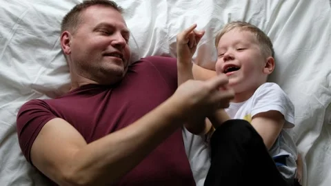 Happy father having fun on a bed with his son child, laughing. View from above Stock Footage 132377763