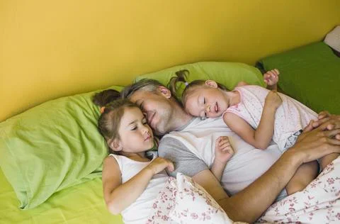 A happy father is lying in bed with two young daughters. rest and relaxation Stock Photos