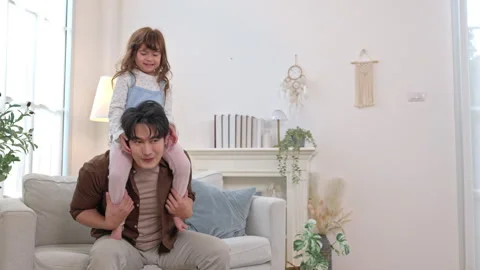 Happy father sitting on the sofa with his daughter on his shoulders Stock Footage 338425791