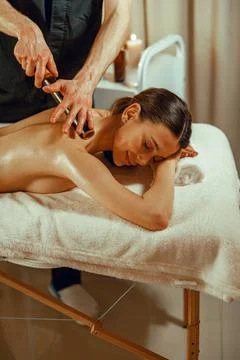 Happy female client getting back massage with hollow bamboo canes at spa salon Stock Photos