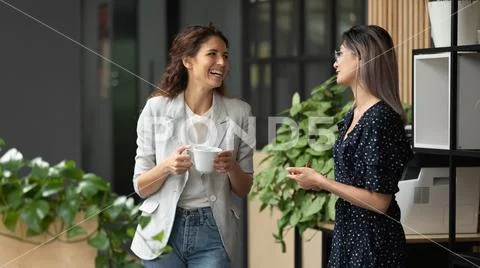 Happy female colleagues talking laughing during break in work space Stock Photos