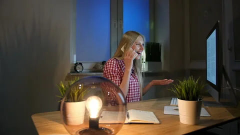 Happy female at computer talking on smartphone. Cheerful amazed blond woman in Stock Footage 155809840