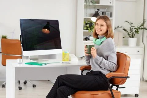 Happy female programmer with computer, cup of coffee and headphones working i Stock Photos